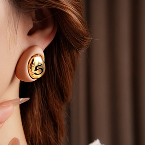 Close-up of gold-plated drop earring with beige enamel and black number five on model