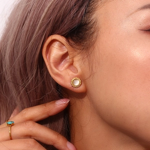 Close-up of golden sunburst stud earrings with white cat-eye stone on a model's ear