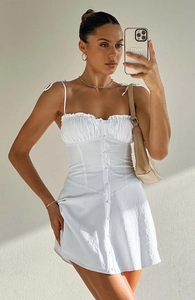 Détail robe courte blanche à fines bretelles avec poitrine froncée et boutons avant