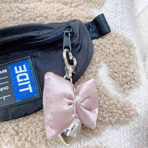Detail of pink silk bow and silver metal heart charm on a black nylon waist bag