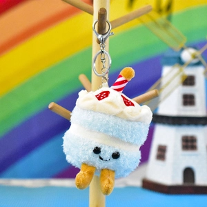 Close-up of a cute blue cake plush keychain with strawberry details and a smiley face.