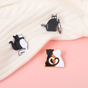 Détail de mignonnes épingles en émail de chats noir et blanc sur un pull en maille