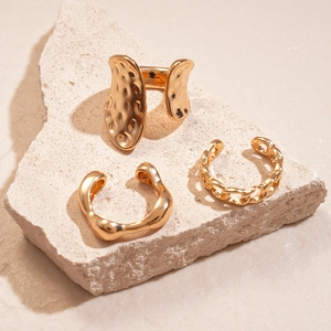 Detail of three gold irregular geometric rings displayed on a natural stone surface