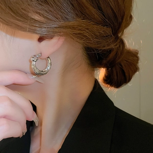 Close-up of silver multilayer twist hoop earrings on a model wearing a black blazer