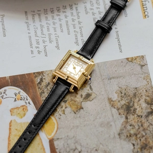 Detail of vintage square gold watch with blue gemstone crown and black leather strap