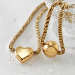 Minimalist gold mesh chain necklace featuring hollow heart and sphere pendants on white base