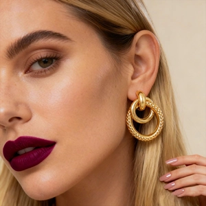 Close-up of golden geometric hollow interlocking earrings worn by a model in soft light
