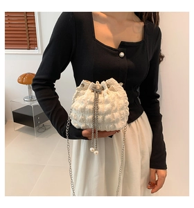 Close-up of white pleated bucket bag featuring a silver chain strap and pearl charm