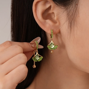 Detail showing a ginkgo leaf earring with green stone on a model wearing golden jewelry