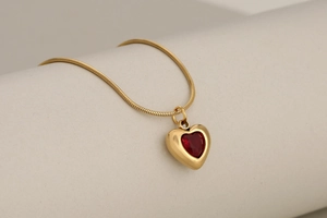 Macro shot of gold snake chain necklace with a ruby red crystal heart pendant