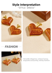 Detail view of large brown glitter heart earrings with gold plating on beige texture