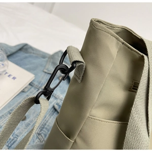 Close-up of black metal swivel hook and strap detail on a light green canvas tote bag