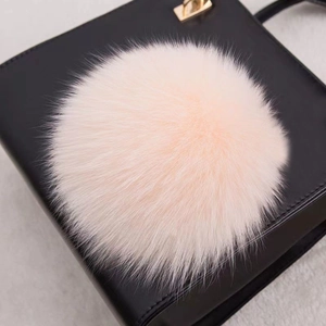 Gros plan d'un pompon en fourrure pêche attaché à un sac à main en cuir noir