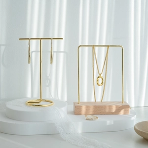 Gold jewelry set with earrings, necklace, and ring displayed on a modern minimalist metal stand