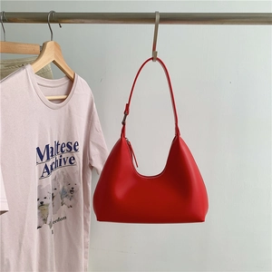 Close-up of red PU leather underarm bag hanging on a rack with a casual outfit background