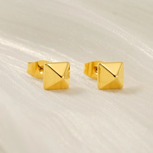 Macro view of 18k gold plated pyramid stud earrings on white silk fabric background