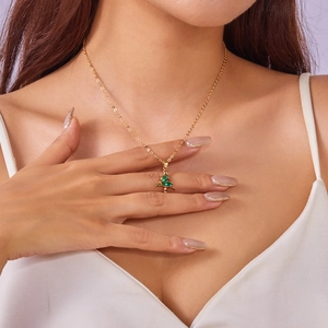 Detail of model wearing a gold necklace featuring a green stone Christmas tree pendant