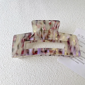 Macro detail of a square marbled purple acetate hair claw clip on a white textured surface