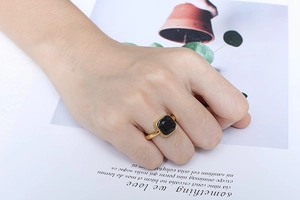 Detail shot of a square black gemstone ring in gold finish worn by a model