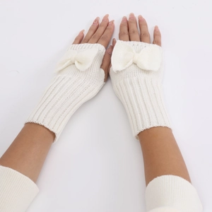 Close-up of white knitted fingerless gloves with a decorative bow and ribbed texture