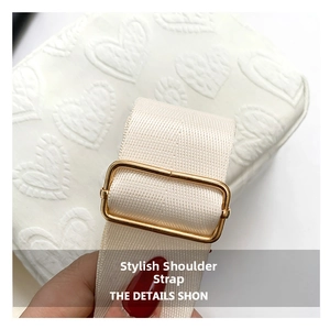 Close-up of wide nylon strap with gold metal buckle and heart-embossed cream leather