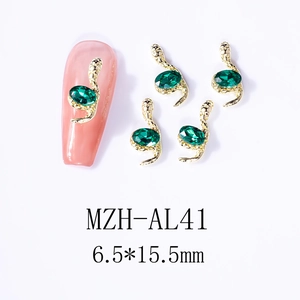 Macro detail of snake-shaped nail charms with emerald stones and gold metal finish