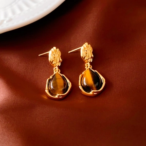 Detailed close-up of vintage gold teardrop earrings with tiger eye stone on silk fabric