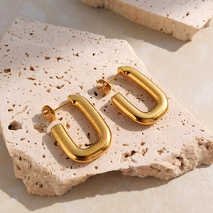 Gros plan de boucles d'oreilles en U en acier titane doré sur une pierre beige
