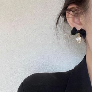 Détail d'une boucle d'oreille nœud en velours avec perle cœur portée par un modèle
