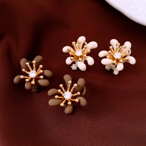 Dettaglio orecchini a fiore placcati in oro con petali marroni e bianchi su seta