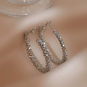 Textured silver hoop earrings with a shimmering finish on elegant pink satin fabric