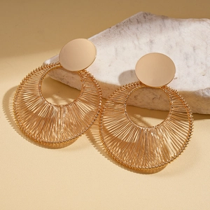 Close-up of golden metal wire fan-shaped woven earrings on an elegant stone base