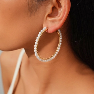 Detail view of a large gold-tone hoop earring featuring elegant rows of white pearls
