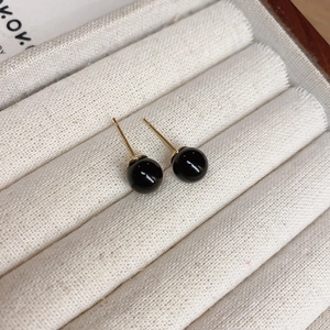 Macro shot of minimalist black bead stud earrings with golden needles on fabric