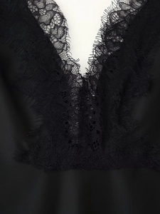 Makro-Detail der exquisiten Wimpernspitze an einem schwarzen Seiden-Satin-Kleid