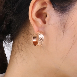 Close-up of gold wide C-shape earrings with textured grid pattern worn on woman's ear