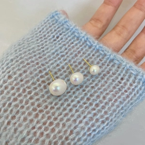 Three sizes of elegant pearl earrings with golden pins on blue knit background