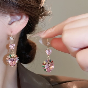 Detail of pink heart zircon earrings with gold plating on model and held by hand
