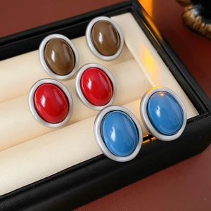 Close-up of three pairs of oval earrings in brown, red, and blue on a velvet display tray