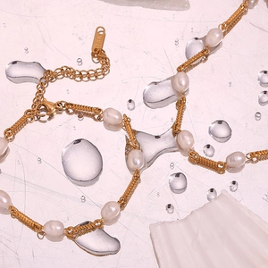 Macro detail of 18K gold-plated chain with freshwater pearls on a wet pink mirror surface