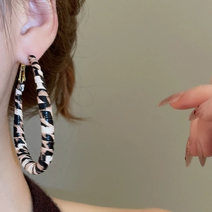 Detail of leopard print woven hoop earring with gold clasp shown on a model's ear