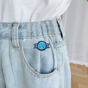 Blue enamel ribbon brooch featuring It's fine text pinned on denim pocket