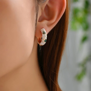 Close-up of white enamel flower hoop earrings with green clover pattern on ear