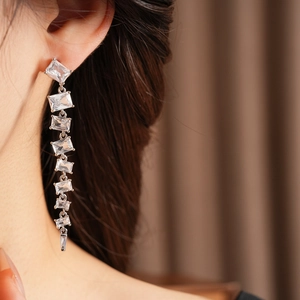 Close-up of dangling silver tassel earrings with sparkling square cubic zirconia stones