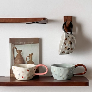 Detail of irregular ceramic mugs with hand-painted animal patterns on wooden shelves
