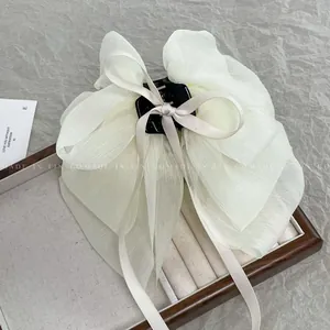 Detail of a cream chiffon bow hair claw clip with layered fabric and a plastic grip