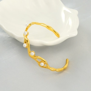 Detailed close-up of a gold wave bangle with pearls on a shell porcelain dish