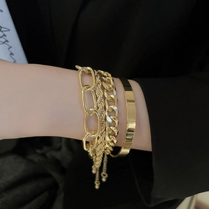 Gold layered metal chain and bangle set worn over a black blazer sleeve
