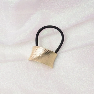 Detailed shot of gold brushed metal cuff on a black elastic hair tie for ponytails