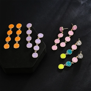 Detailed view of colorful enamel smiley face long drop earrings on a black display stand